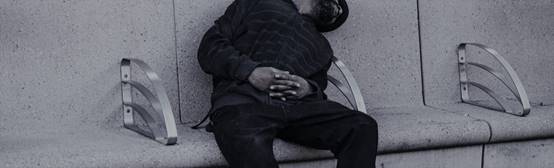 Hostile architecture: a homeless man asleep on a bench with arms dividing the length of the bench