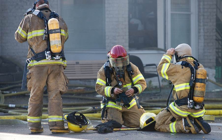 Firemen wearing protective gear sitting on the ground
Description automatically generated